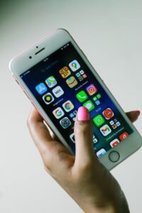 Close-up of a hand holding a smartphone displaying various apps on the screen.